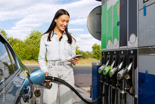 Foto Smiling lady refueling her car and messaging on smartphone at the petrol station