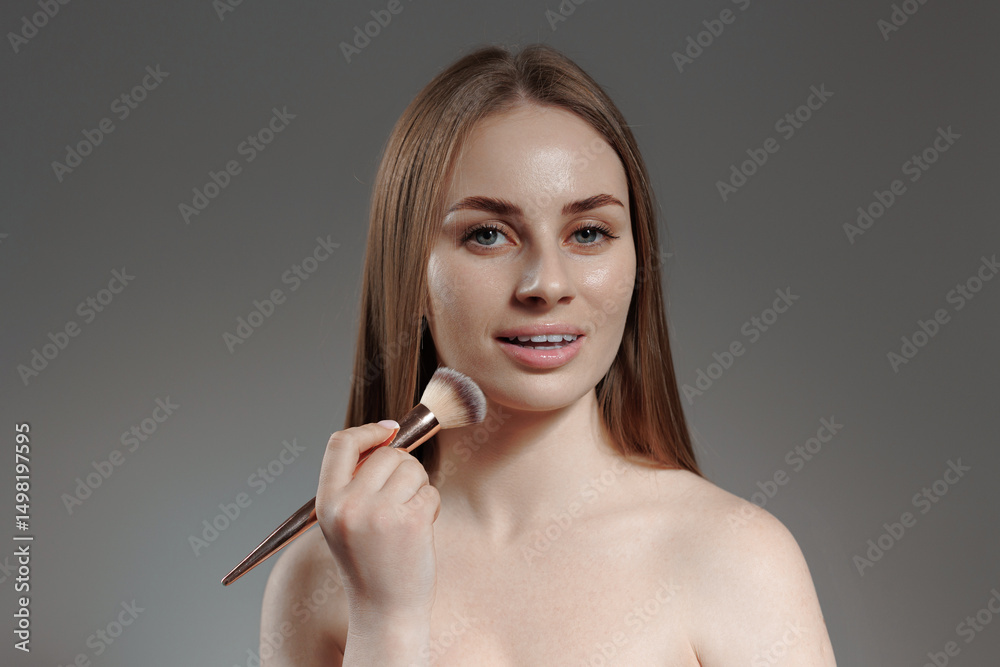 Obraz premium Model applying makeup with a brush in a studio setting during a beauty photoshoot session
