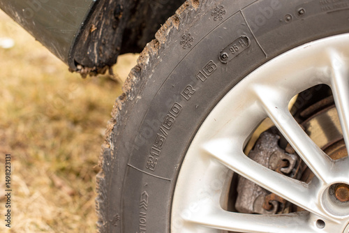 Close-up of an alloy wheel and a 215 – 60 R16 winter tire with a rugged tread pattern. Tire has a 95H index. Visible mud stains and dirt.