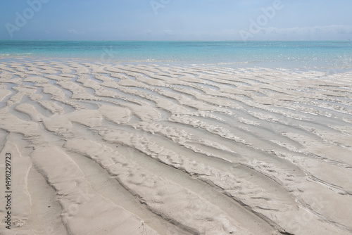 Gentle ripples on the soft white sand. A shallow sandbank near Mnemba Island, Zanzibar, Tanzania. Sunlit shallow waters close to the coral reef on the northeastern coast of Zanzibar.