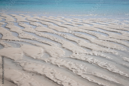 Gentle ripples on the soft white sand. A shallow sandbank near Mnemba Island, Zanzibar, Tanzania. Sunlit shallow waters close to the coral reef on the northeastern coast of Zanzibar.