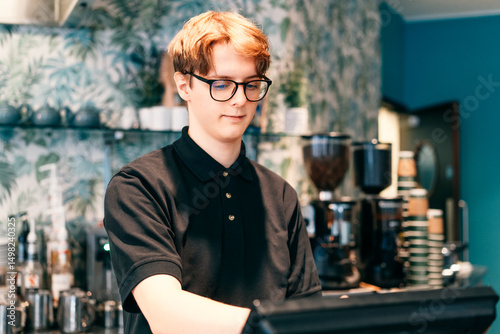 Young waiter serving customer at cash point in cafe. Man working with POS terminal. Cashier, barista checking for payment receipt. Hospitality, server and preparing a slip at the till in coffee shop
