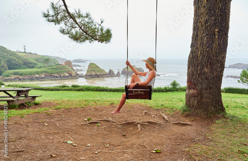 Tourist on a swing at Porcía beach, El Franco, Asturias, Spain.