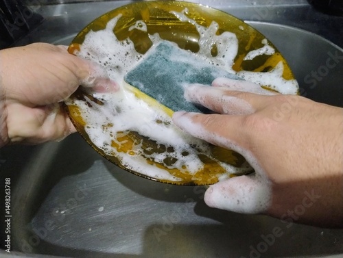Hand with a sponge washing a plate.