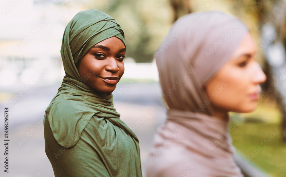 Fototapeta premium Two Diverse Muslim Women Posing Wearing Traditional Hijab Headscarf Looking At Camera Standing Outdoors. Diversity And Unity Of Islamic Females Concept. Selective Focus