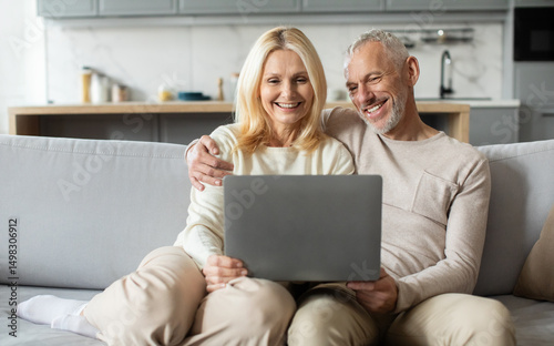 A senior couple relaxes on a comfortable couch, sharing laughter while looking at a laptop in their beautifully designed living room. The warm atmosphere highlights their happiness and connection.