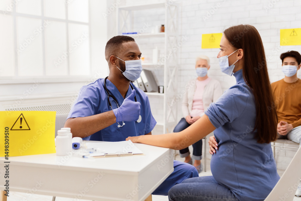 Fototapeta premium Successful Coronavirus Vaccination. Doctor In Face Mask Gesturing Thumbs-Up To Vaccinated Against Corona Virus Female Patient Sitting In Hospital. Covid Vaccine Injection And Immunization Campaign