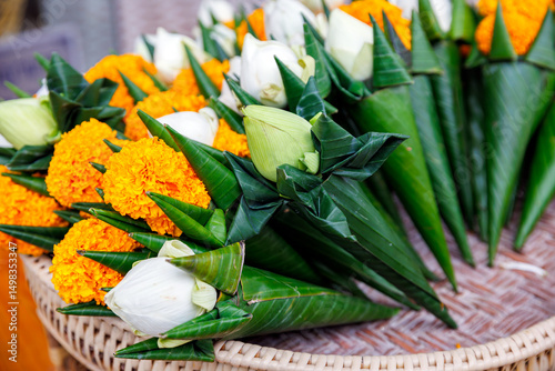 Traditional Thai floral offerings for the Inthakhin pillar ceremony at Wat Chedi Luang, Chiang Mai, featuring lotus buds and marigolds in banana leaf cones.