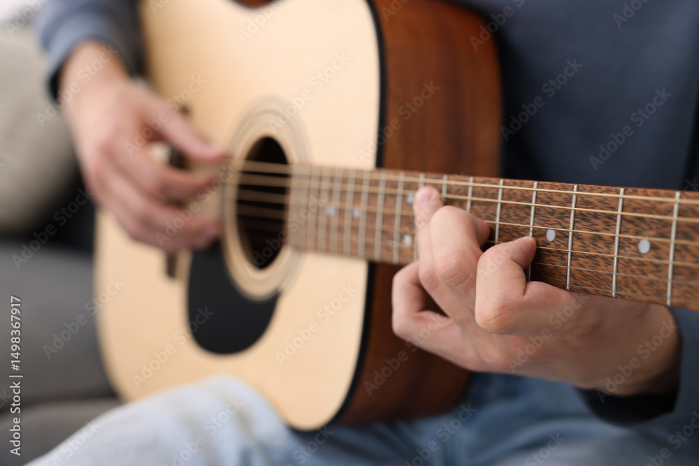 Fototapeta premium Young man playing guitar on sofa indoors, closeup