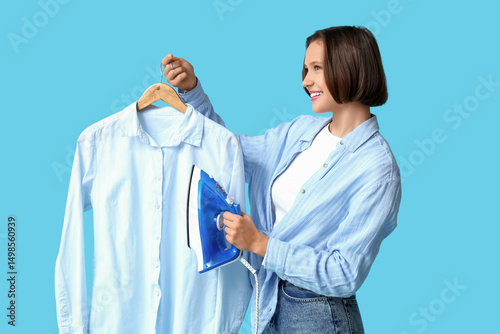 Smiling young woman with iron and shirt on blue background