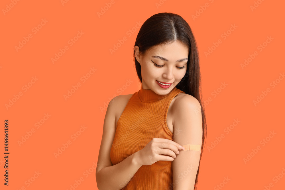 Obraz premium Young Asian woman with applied medical patch on orange background. Immunization concept