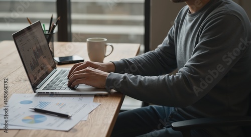Man working on laptop at wooden desk with documents and coffee  