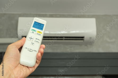 Man's hand using remote control open The air conditioner is cooled to 25 degrees Celsius in his bedroom. Health concepts and energy savings