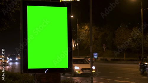 Urban night scene with glowing streetlights, road signs and a large green screen billboard. Concept of digital advertising and nighttime visibility