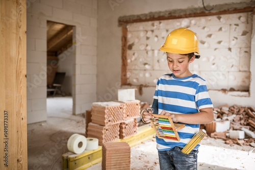 Boy wearing hardhat counting bead of abacus while standing at loft