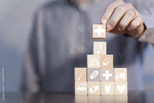 A person's hand placing a wooden block with a medical cross symbol onto a stack of other blocks