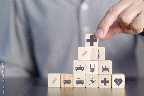 A person's hand placing a wooden block with a medical cross symbol onto a stack of other blocks