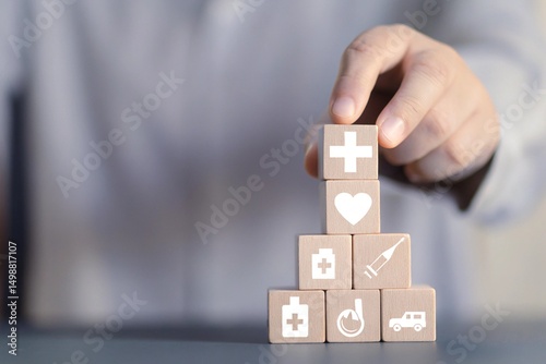 A person's hand placing a wooden block with a medical cross symbol onto a stack of other blocks