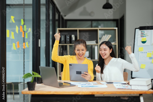 Vászonkép Two excited Asian businesswomen raising their arms and delighted at a successful company event in an office environment