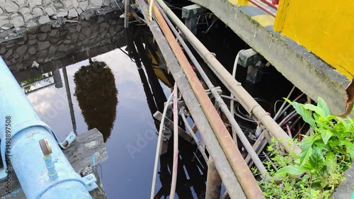 The river water is surrounded by industrial pipes and concrete structures, signifying the challenges of the urban environment and infrastructure elements.