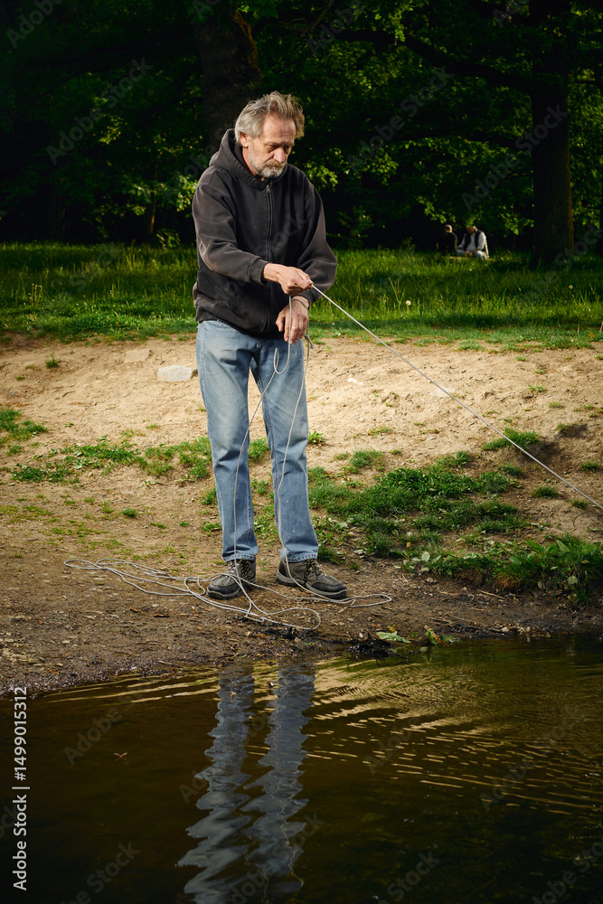Fototapeta premium Senior citizen fishing with magnet in city lake found guns
