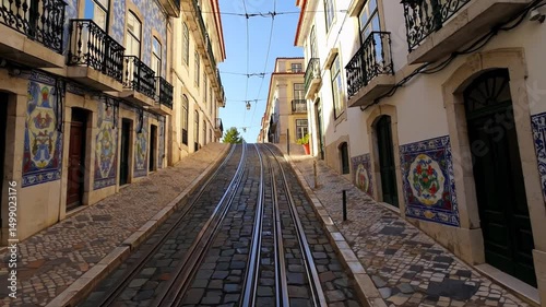 Steep cobblestone tram track street lined with traditional tiled buildings and wrought iron balconies in Lisbon, Portugal

