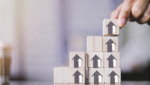 A hand is placing a wooden block with a house icon on top of a stack of blocks