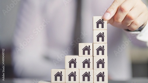 A hand is placing a wooden block with a house icon on top of a stack of blocks