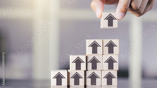 A hand is placing a wooden block with a house icon on top of a stack of blocks