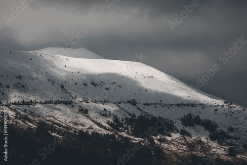 snowy mountain landscape with spotlight in the snow and dark stormy clouds