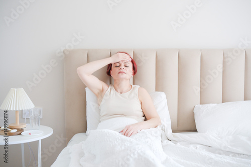 Vászonkép A woman is lying in bed, experiencing a persistent headache and searching for re