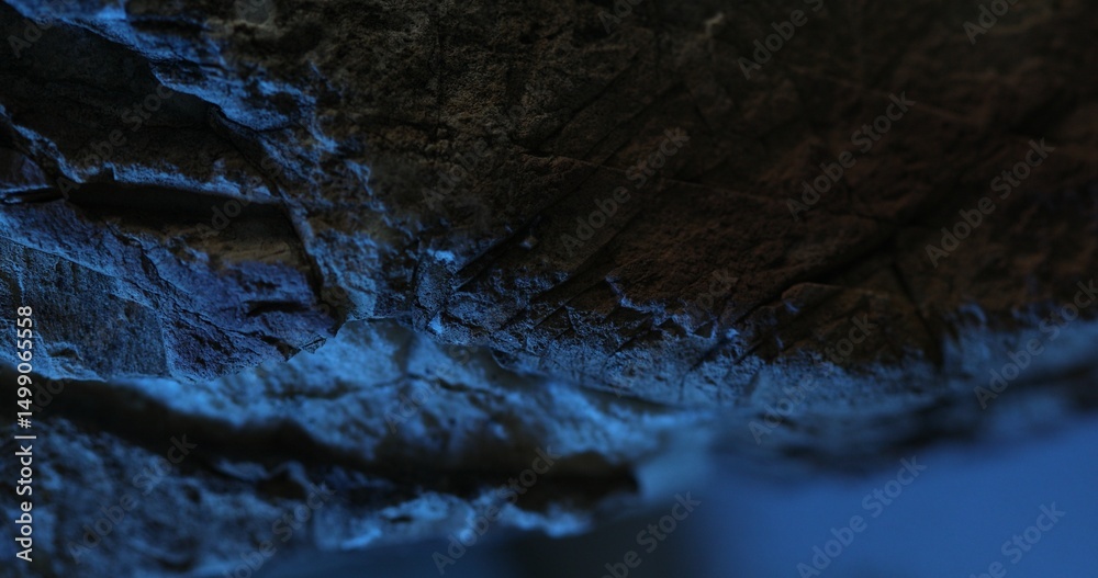 Fototapeta premium Close-up of dark rock surface with vivid blue lighting and layered texture