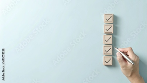 A hand holding a pen is checking off wooden boxes on a vertical list of square blocks