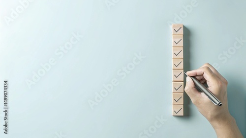 A hand holding a pen is checking off wooden boxes on a vertical list of square blocks