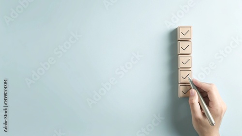 A hand holding a pen is checking off wooden boxes on a vertical list of square blocks