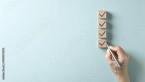 A hand holding a pen is checking off wooden boxes on a vertical list of square blocks