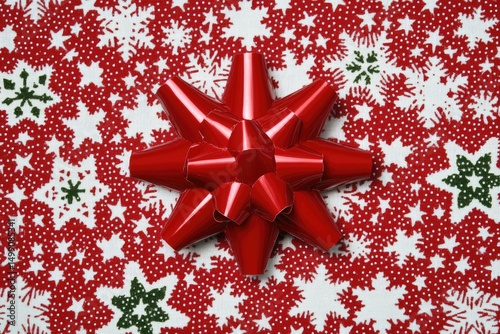 Red star-shaped gift bow on a festive red and white fabric with snowflakes and stars photo