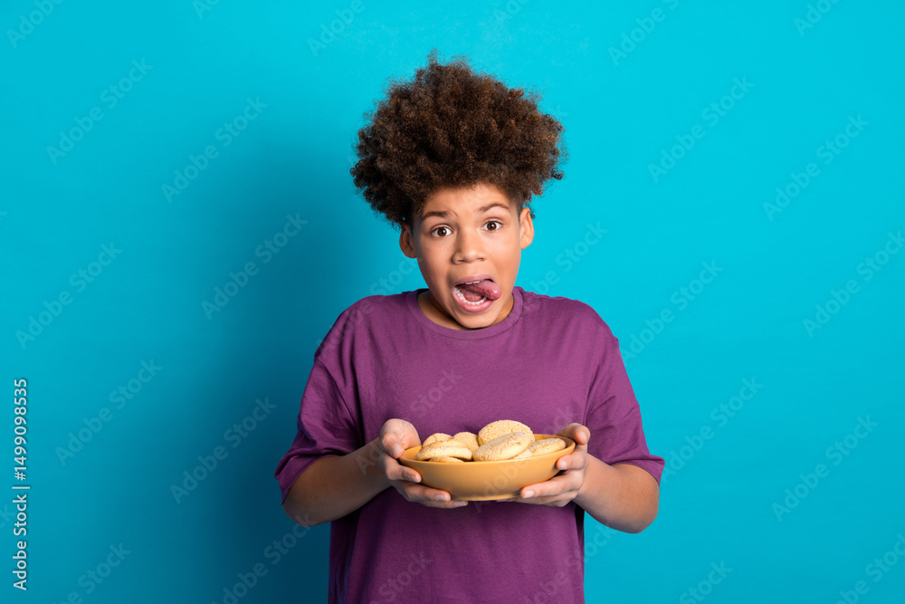 Cheerful boy holding a bowl of cookies against a vibrant blue background expressing a playful mood Cheerful boy holding a bowl of cookies against a vibrant blue background expressing a playful mood