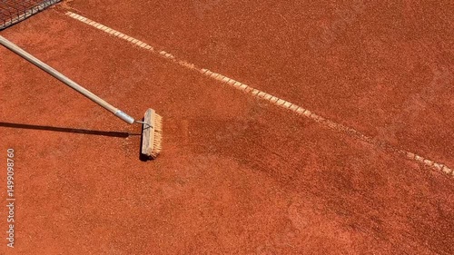 person sweeping debris from a clay tennis court with a large broom, maintaining the playing lines, concept of sports maintenance, club management, facility care