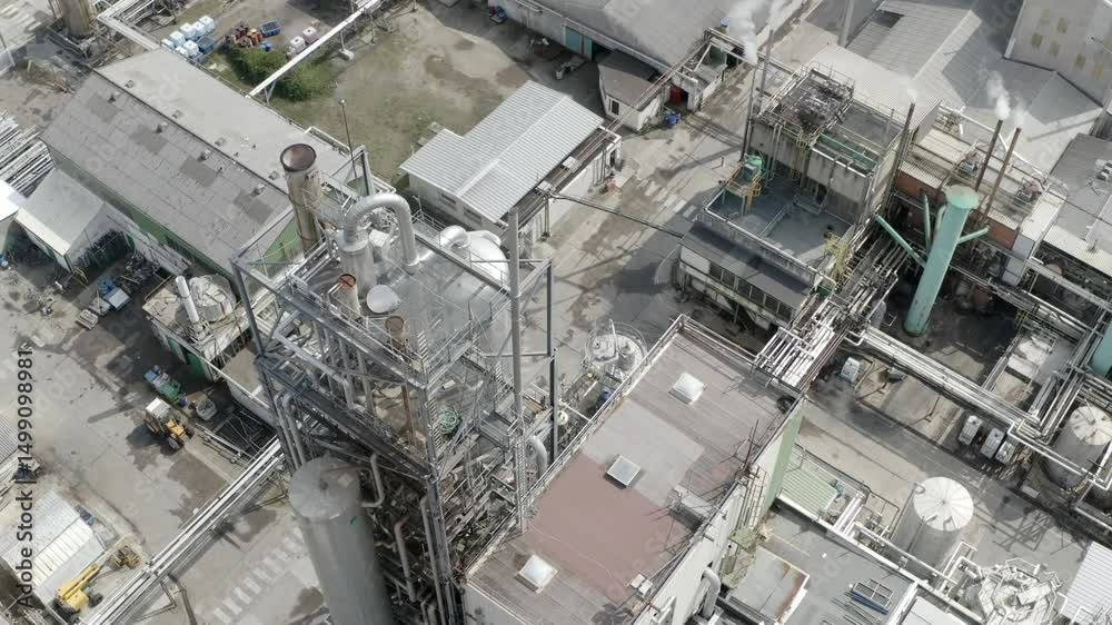 Aerial drone view of a specific section of DRT Factory, highlighting rooftops, extensive piping, and adjacent trees in Veille-Saint-Girons, France