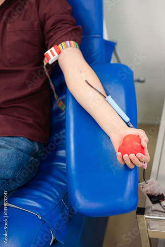 Man Donating Blood with Red Heart Stress Ball. Close-up of a male blood donor sitting in a medical chair, holding a red heart-shaped stress ball during the donation process