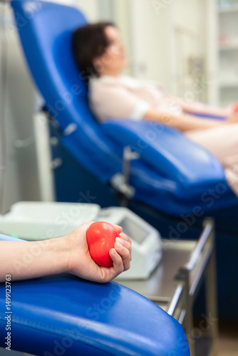 Blood Donation in Progress with Focus on Red Heart Stress Ball. Close-up of a donor’s hand holding a red heart-shaped stress ball during a blood donation session