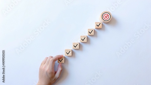 A hand places a circular block with a target icon at the end of a sequence of wooden blocks with checkmarks