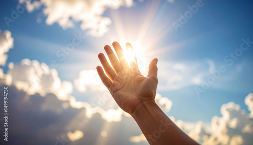 Reaching for the light: A single hand reaches towards the bright sunlight, a beacon of hope against a backdrop of puffy clouds and a vibrant blue sky.