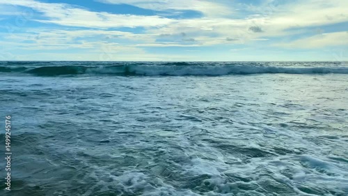 Calm ocean waves gently roll toward the shore, creating a tranquil and soothing scene. The deep blue of the water contrasts beautifully with the white caps of the waves