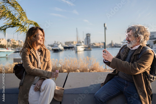 Photography Senior man taking photos of woman eating ice cream at the port