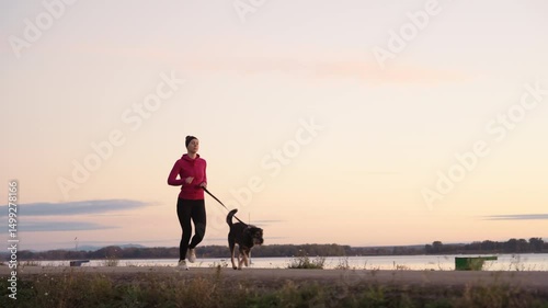 A woman is jogging alongside her dog during the breathtaking sunrise by the water