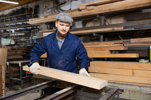 Wallpaper Mural Young man worker in carpentry workshop putting wooden board on cutting machine Torontodigital.ca