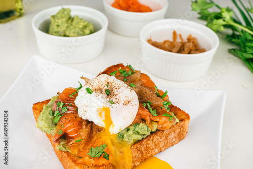  fresh breakfast plate with poached eggs, flowing yolk, smoked salmon guacamole on toast homemade healthy and served on bread.