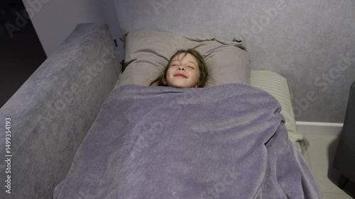 A cheerful little girl lies down in bed and tries to fall asleep